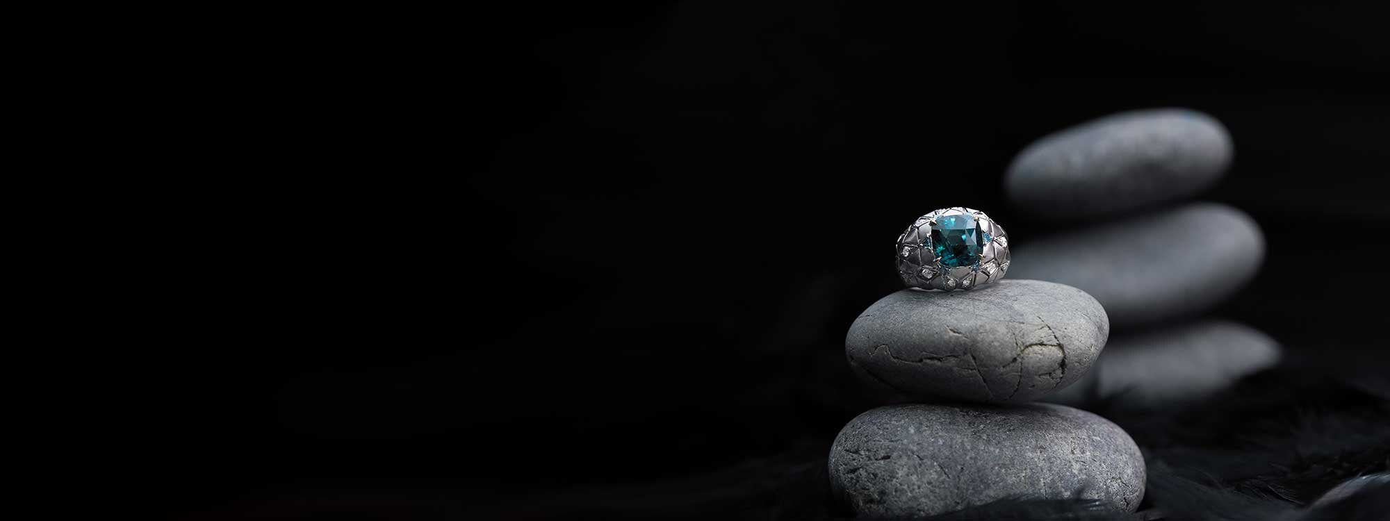 Blue-green gemstone ring resting on smooth dark stones